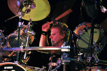 A man playing drums on stage with other people.