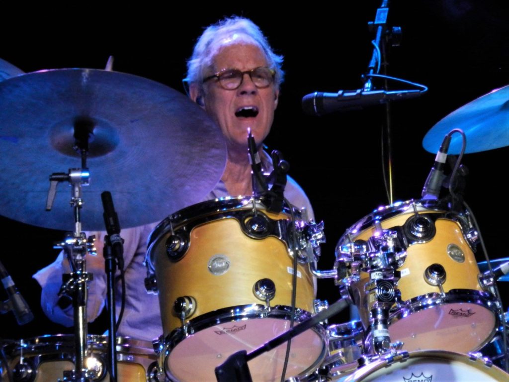 A man with glasses is playing drums on stage