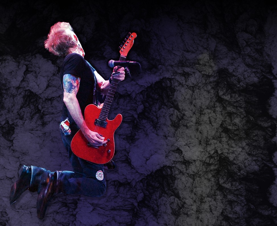 A man jumping in the air with a guitar.