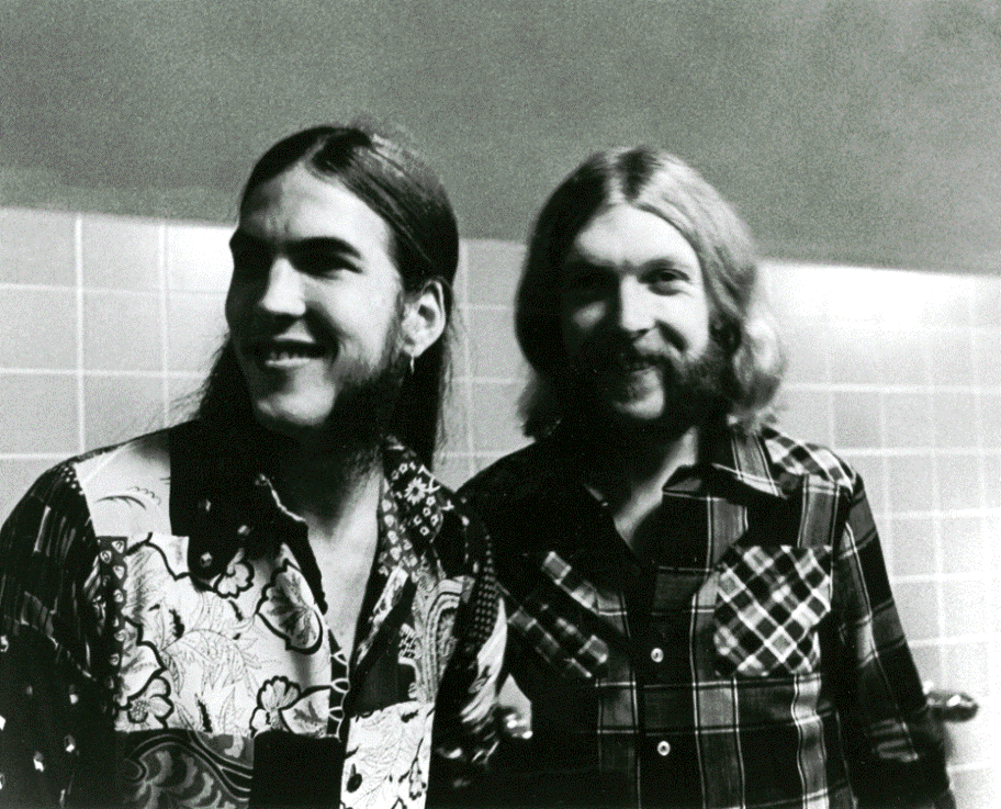 Two men standing next to each other in front of a wall.