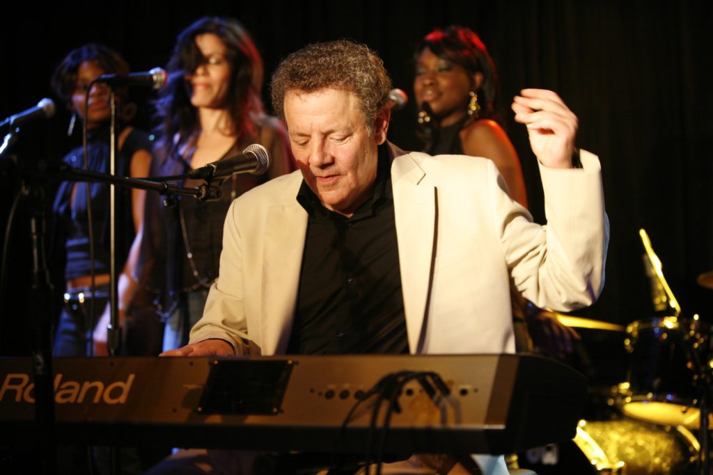 A man playing the piano while two women sing.