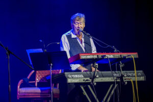 A man playing the keyboard on stage with other people.
