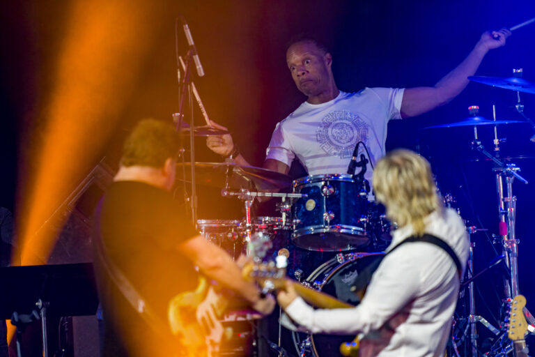 A man playing drums with two other people.