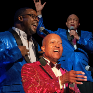 Three men in suits singing on stage